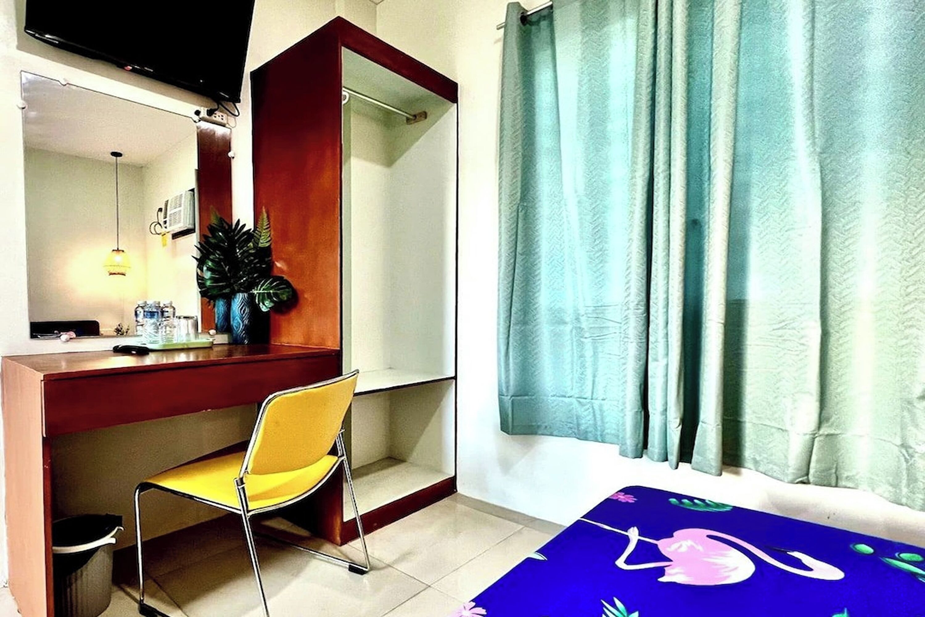 Une chambre avec un bureau, une chaise, un lit recouvert d’une couvre-lit à motifs floraux, une douche et un rideau.