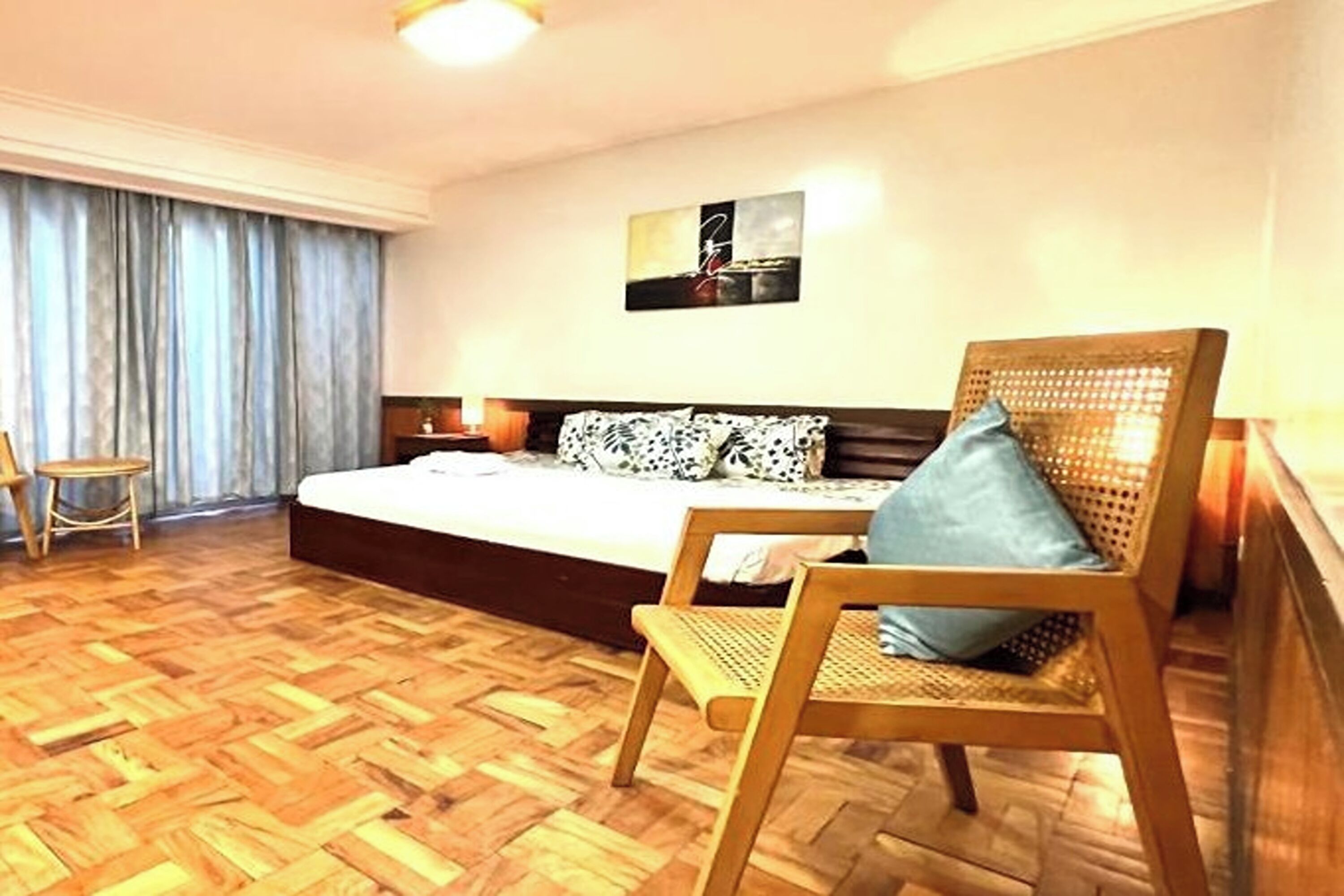 Un dormitorio con una cama grande, suelo de madera, una silla y una obra de arte colgada en la pared.