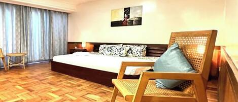 Un dormitorio con una cama grande, suelo de madera, una silla y una obra de arte colgada en la pared.
