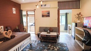 A cozy hotel room with a bed, a sofa, a small table, and a TV. There is a window with curtains and a view of the outside. - Blockhouse Samui (Koh Samui)