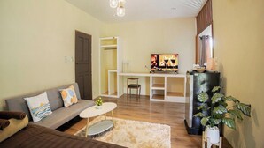 A living room with a sofa, coffee table, and a TV on a stand. There is a plant and a window with curtains. - Blockhouse Samui (Koh Samui)