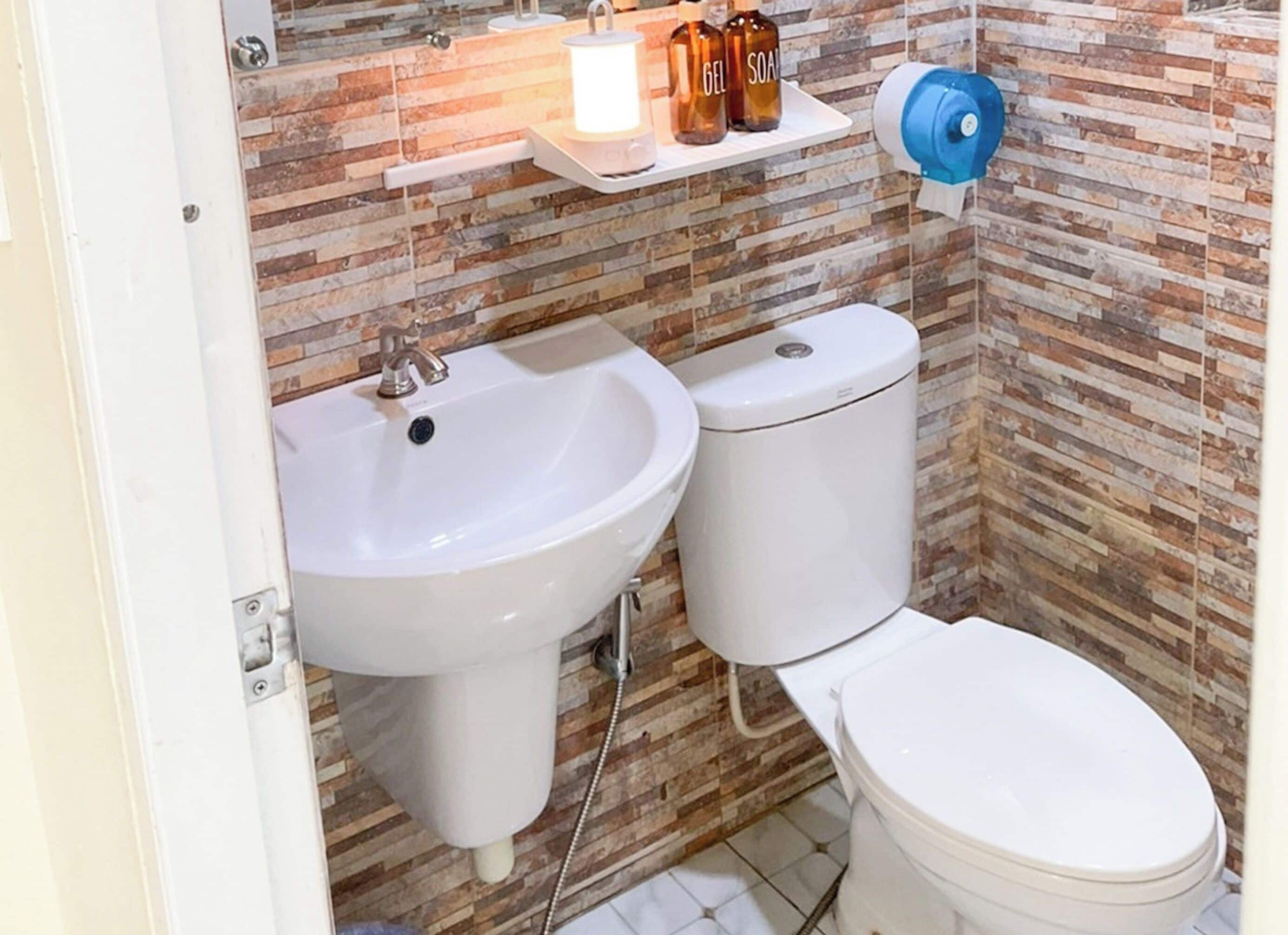A bathroom with a white sink, toilet, and a shelf with toiletries.