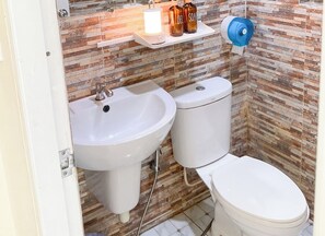 Un baño con lavamanos blanco, inodoro y estante con artículos de aseo.