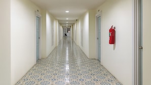 A long, narrow hallway with patterned floor tiles, doors on both sides, and a fire extinguisher mounted on the wall. - Jommalai Boutique Hotel (Phitsanulok)