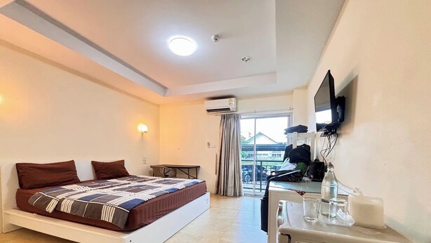 A hotel room with a bed, a desk, a refrigerator, and a window with a view of the outside. - Jommalai Boutique Hotel (Phitsanulok)