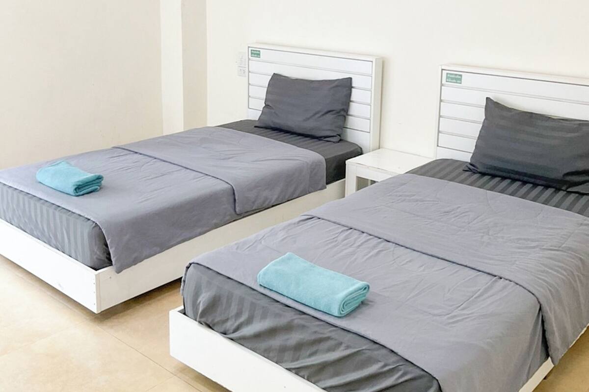 Two single beds with grey bedding and blue towels, white headboards, and a small bedside table.