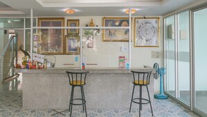 A reception area with a counter, two bar stools, framed artwork on the wall, and a staircase to the left. - Jommalai Boutique Hotel (Phitsanulok)