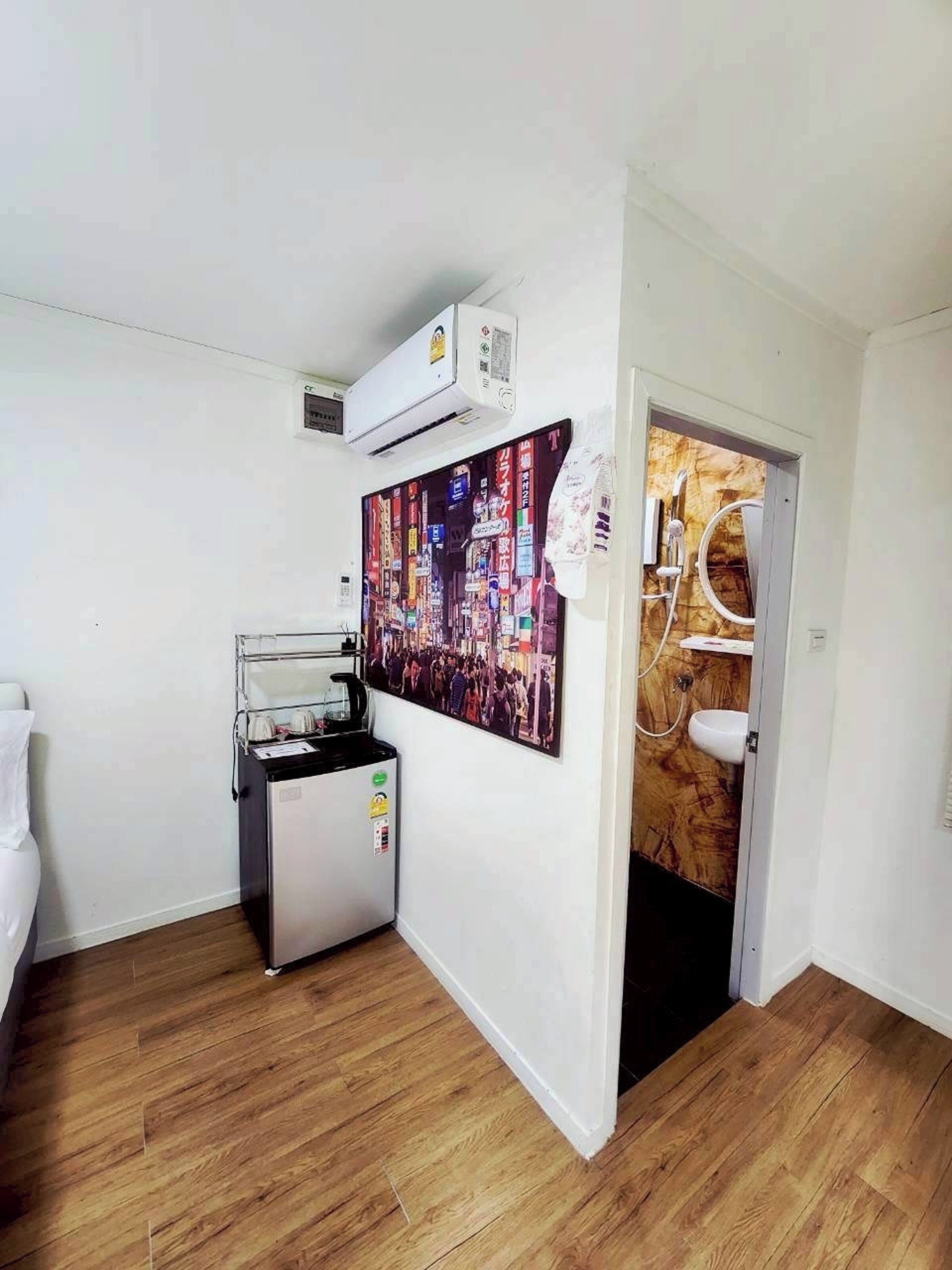Quarto de hotel pequeno com chão de madeira, cozinha compacta, casa de banho e zona de duche.