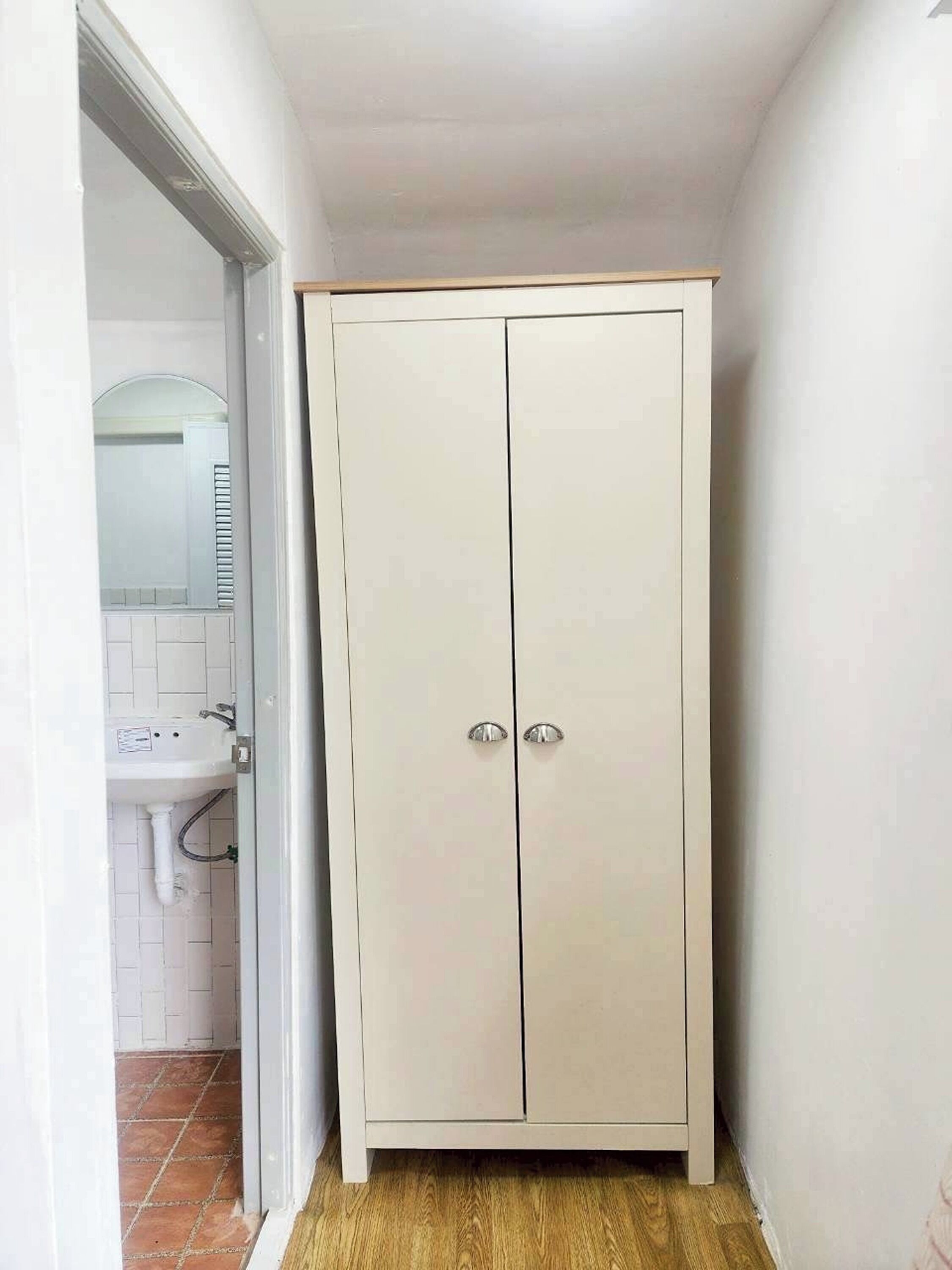 A narrow hallway with a white wardrobe, a sink, and a mirror.