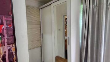Une pièce avec une armoire blanche, un miroir, une fenêtre avec des stores et un rideau.