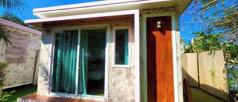 Una casa pequeña de un solo piso con techo plano, puerta principal y puerta corrediza de vidrio.