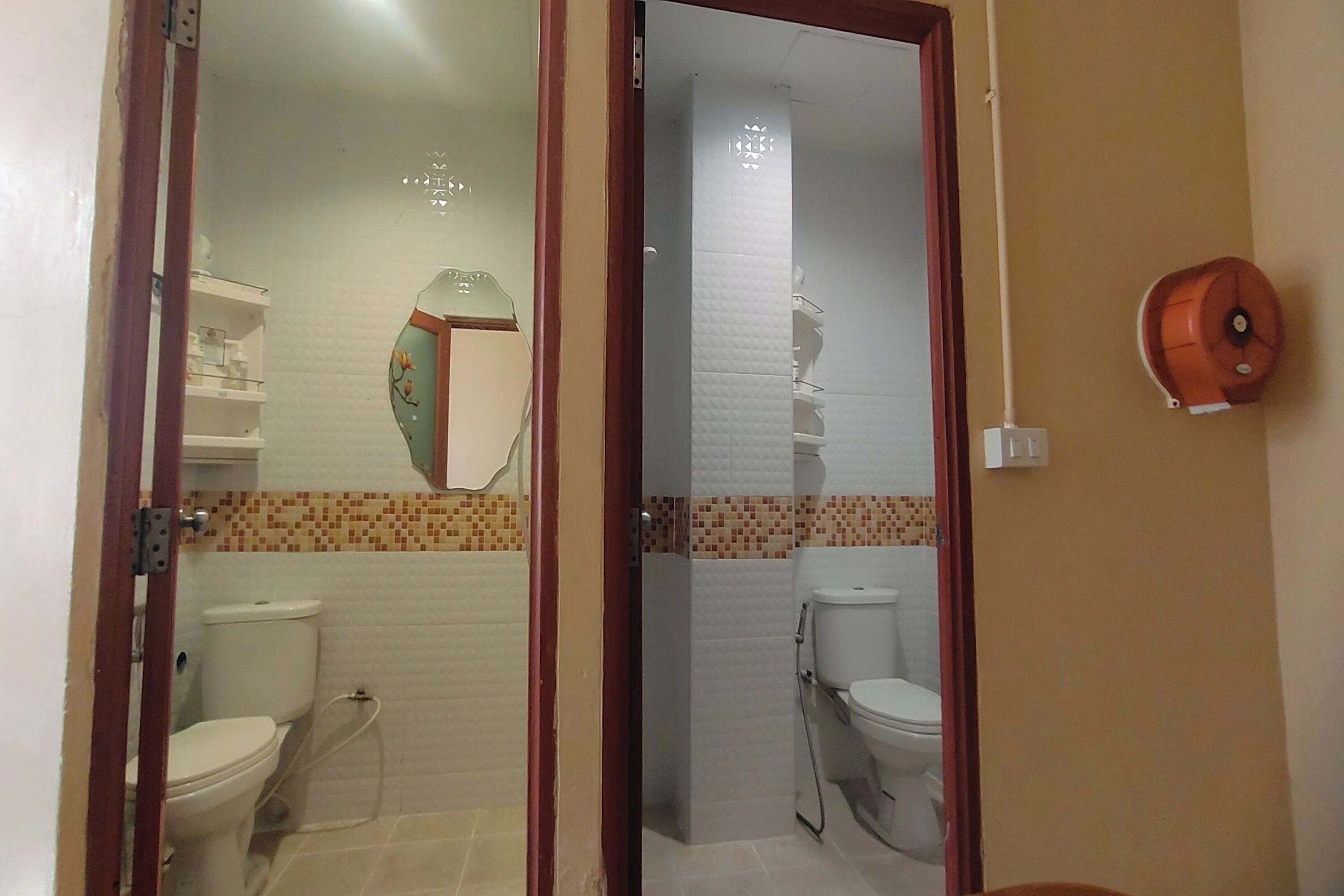 Ein Badezimmer mit zwei Toiletten, einer Dusche und einer gefliesten Wand mit einem dekorativen Muster.