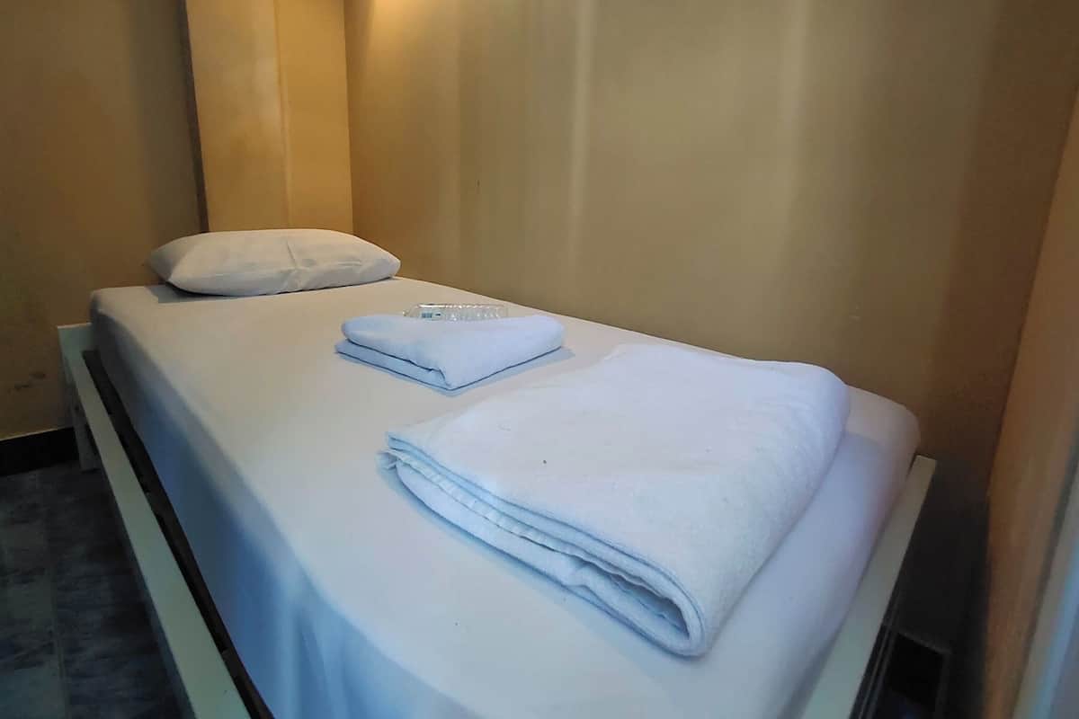 A neatly made bed with a folded white towel and a remote control on it.