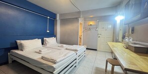 Hotelkamer met twee bedden, een houten tafel, een stoel, een deur en een wandlamp.