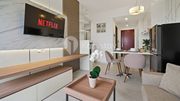 Egy modern nappali, melyben egy síkképernyős televízióban a „NETFLIX” felirat látható, egy fa kávéasztalon virágos növény áll, van egy kanapé, és egy étkezősarok székekkel.