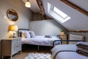 Et soveværelse med skråvæg, ovenlys, en seng med puder, et natbord med lampe, en radiator og en lille plante.