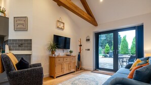 A modern living room with a wooden ceiling, a flat-screen TV, a wooden cabinet, and a blue sofa. - Beautiful 2 Bedroom Barn in Cerney Wick (Cerney Wick)