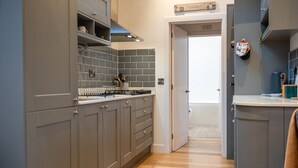 A kitchen with grey cabinets, a tiled backsplash, and a wooden floor. - Beautiful 2 Bedroom Barn in Cerney Wick (Cerney Wick)