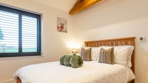 A bedroom with a large bed, a window with blinds, a wall-mounted lamp, and a framed picture. - Beautiful 2 Bedroom Barn in Cerney Wick (Cerney Wick)