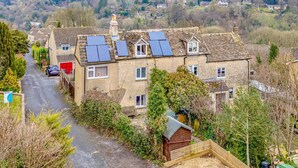 Une maison traditionnelle en pierre, dotée de panneaux solaires sur le toit, entourée de verdure et s’intégrant dans un paysage rural.