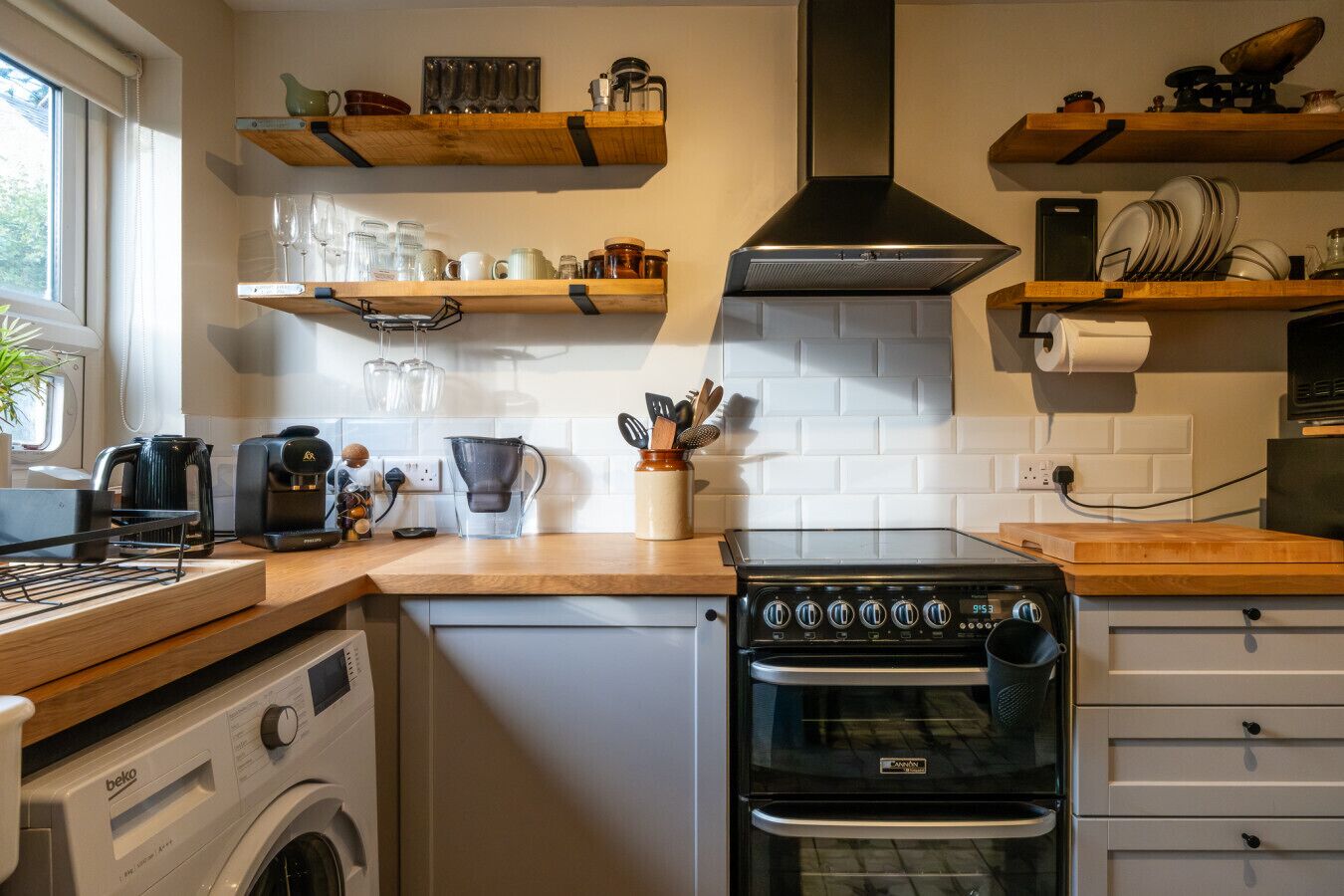A compact kitchen with a built-in washing machine, a stove, and wooden shelves above the counter.