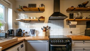 Une cuisine compacte équipée d’un lave-linge intégré, d’une cuisinière et d’étagères en bois au-dessus du plan de travail.