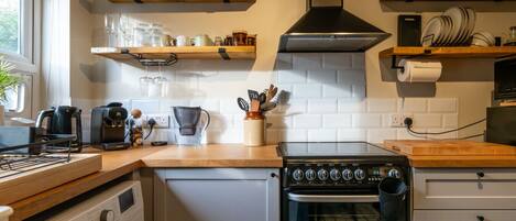 A compact kitchen with a built-in washing machine, a stove, and wooden shelves above the counter.
