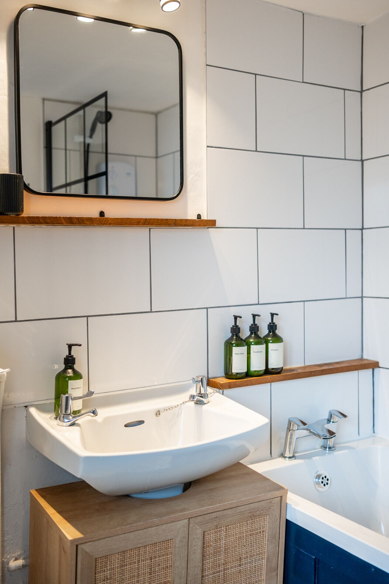 A bathroom with a white sink, a mirror, and a shelf with green bottles.