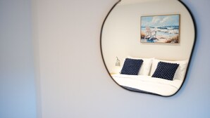 Un dormitorio con cama, dos almohadas, una mesita de noche, una lámpara y un cuadro de una escena de playa en la pared.