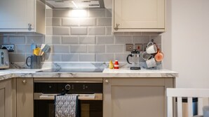 A modern kitchen with a stainless steel range hood, grey tiled backsplash, and a built-in dishwasher. - The Alehouse Retreat, The Crown Inn (Cerney Wick)