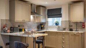 A modern kitchen with marble countertops, a central island with bar stools, and built-in cabinets. - Beautiful One Bedroom Cottage in Cerney Wick (Cerney Wick)