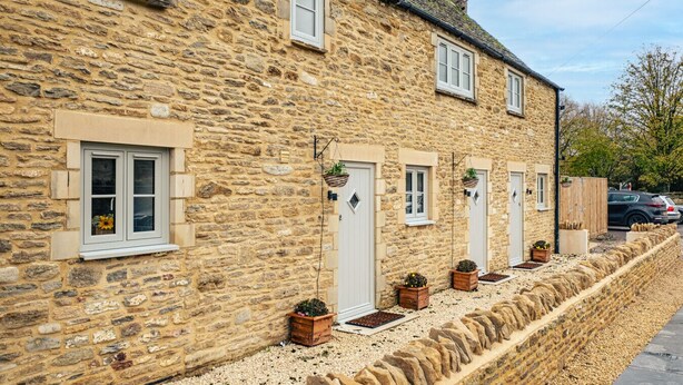 A stone building with multiple windows and doors, some with hanging plants. - Beautiful One Bedroom Cottage in Cerney Wick (Cerney Wick)