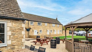 A stone building with a tiled roof, outdoor seating area with tables and chairs, and a covered pavilion. - Beautiful One Bedroom Cottage in Cerney Wick (Cerney Wick)