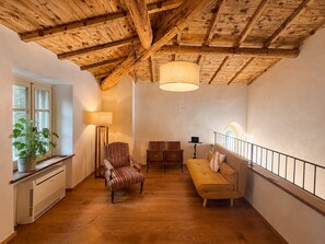 A room with a wooden ceiling, a sofa, a striped chair, a floor lamp, and a potted plant.
