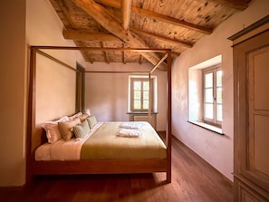A four-poster bed with a wooden frame, a window with a view, and a wooden ceiling.