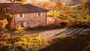 Una casa de piedra con techo de tejas, un pequeño jardín y vistas a un valle y montañas al fondo.