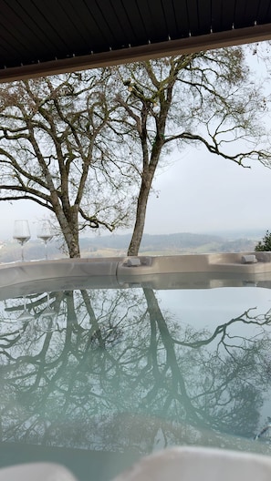 A clear view of a swimming pool with two wine glasses on the edge, surrounded by trees and a distant landscape.
