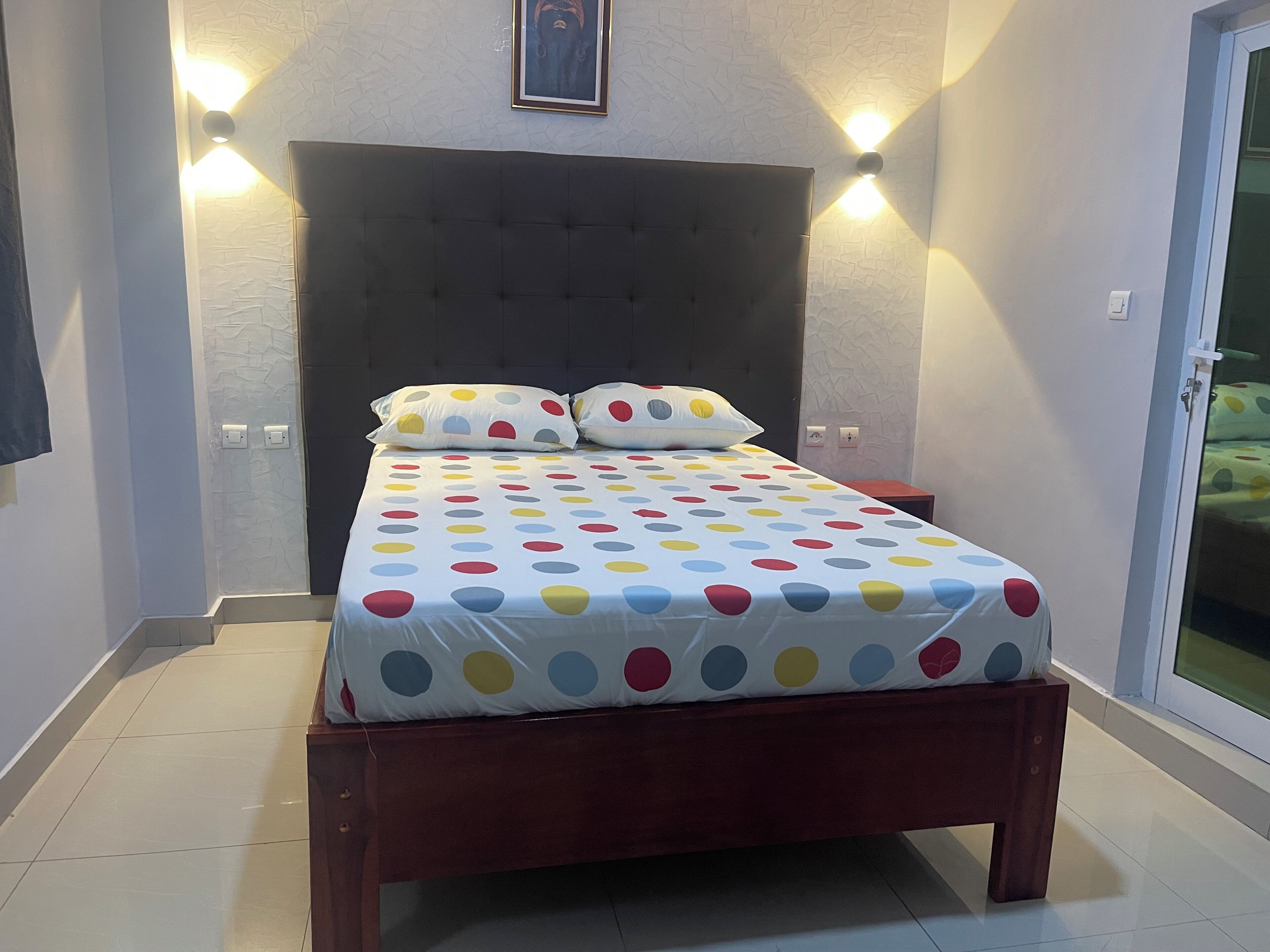 A bedroom with a bed, a headboard, a nightstand, and a wall-mounted light fixture.