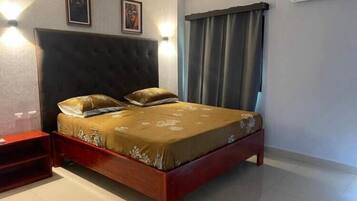 A bedroom with a bed, a nightstand, a wall-mounted air conditioner, and two framed pictures on the wall.