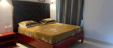 A bedroom with a bed, a nightstand, a wall-mounted air conditioner, and two framed pictures on the wall.