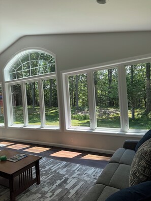 A room with large arched windows, a wooden table, and a grey sofa. - Large home with hot tub in serene wooded setting (Erie)