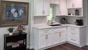 A modern kitchen with white cabinetry, a dark wood floor, a built-in sink, and a coffee maker. - Large home with hot tub in serene wooded setting (Erie)