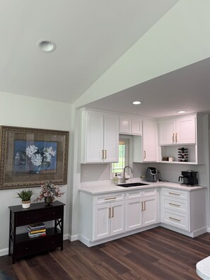 A modern kitchen with white cabinetry, a dark wood floor, a built-in sink, and a coffee maker. - Large home with hot tub in serene wooded setting (Erie)