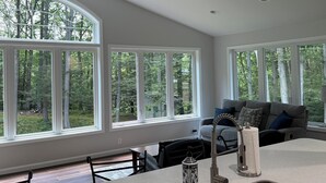 A modern kitchen with a large island, a ceiling fan, and large windows offering a view of a forest. - Large home with hot tub in serene wooded setting (Erie)