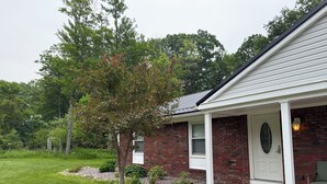 A brick house with a white front door, a small porch, and a well-maintained lawn. - Large home with hot tub in serene wooded setting (Erie)