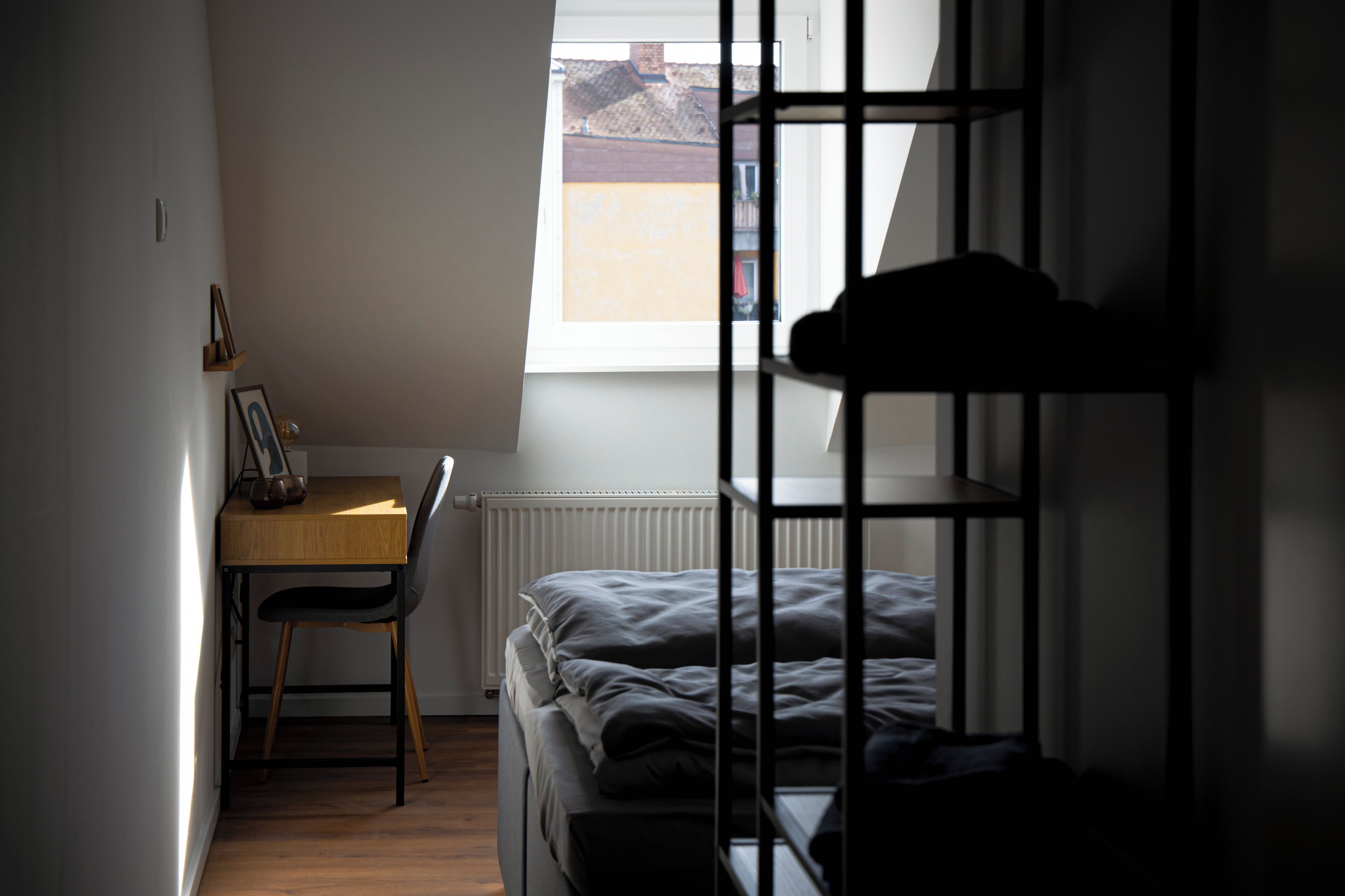 A dormitory room with a bunk bed, a desk with a chair, and a window providing a view of the outside.