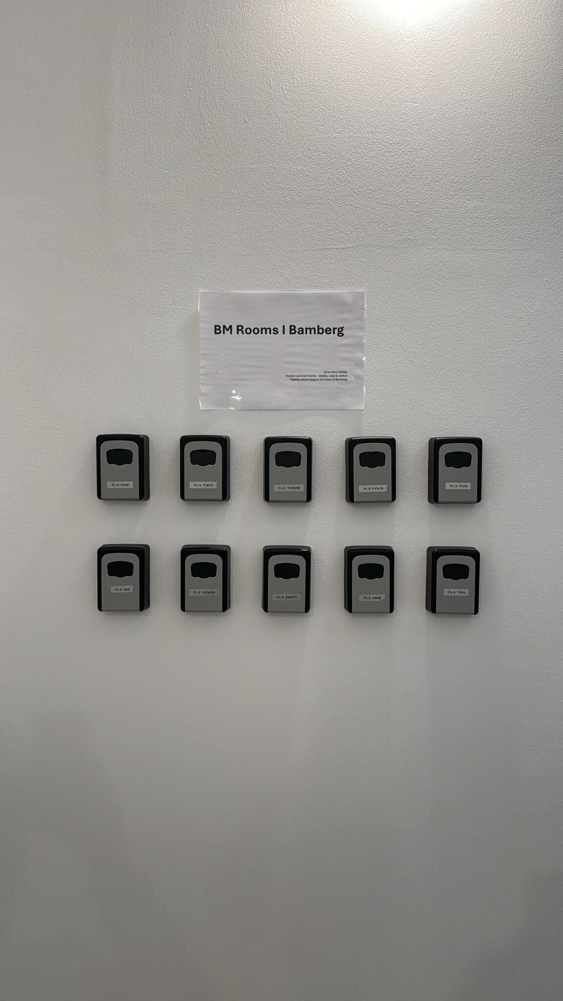 A wall with a sign indicating 'BM Rooms I Bamberg' and a series of room call buttons labeled from 'FLS ONE' to 'FLS TEN'.