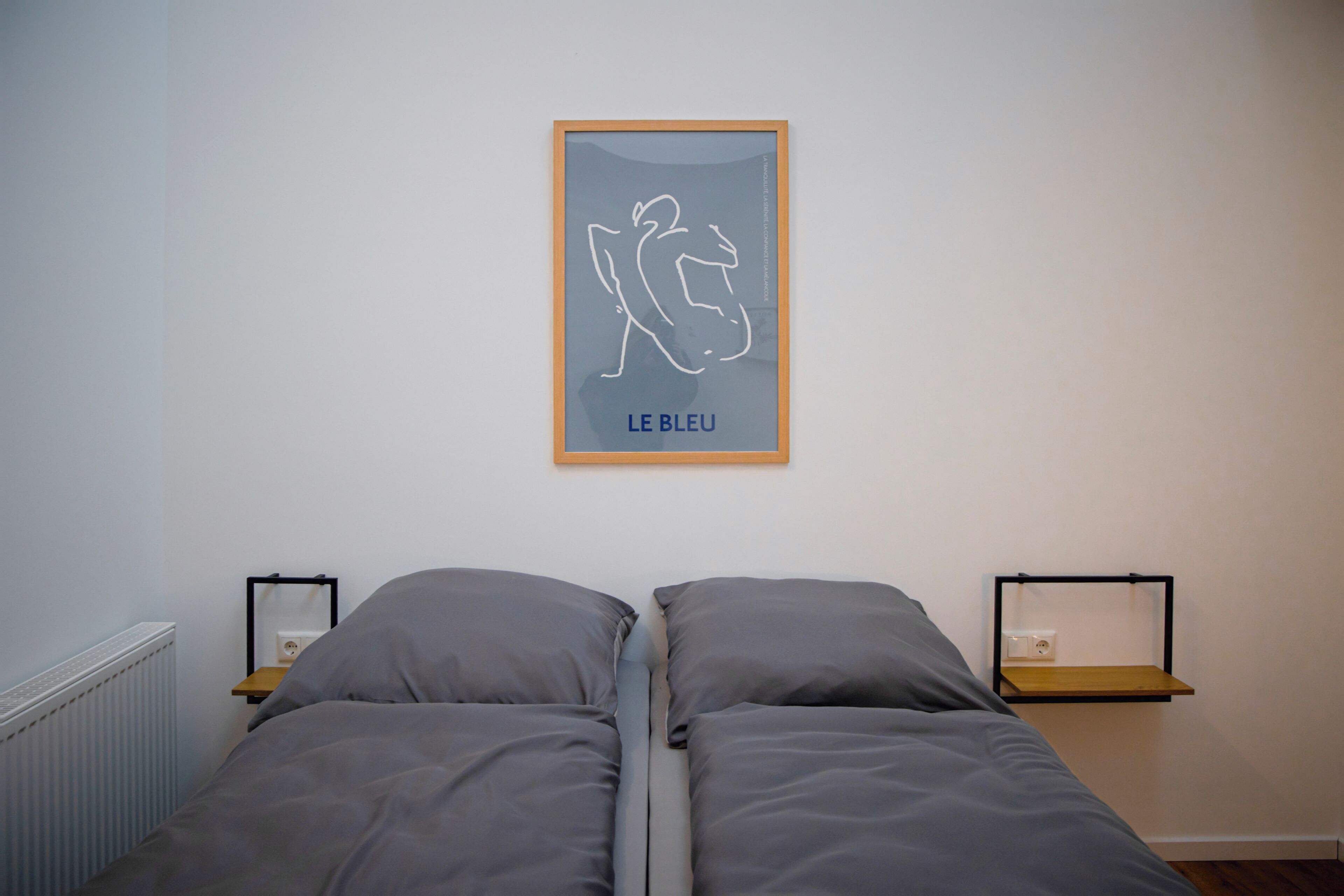 Une chambre à coucher avec un lit, deux tables de chevet, une œuvre d’art encadrée et un radiateur.