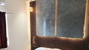 A modern bedroom with a large bed, a marble wall, and a wooden panel design. - J Residency (Pochampalli)