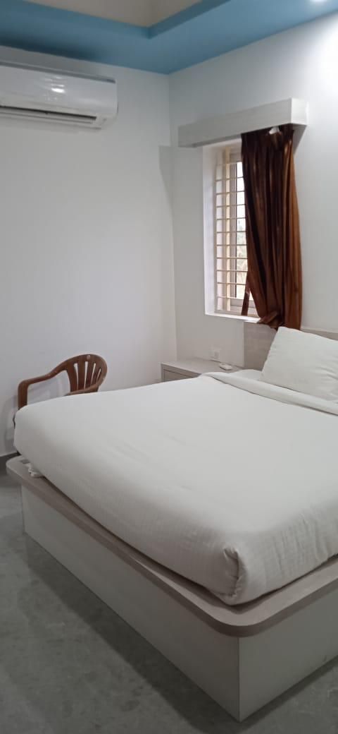 Une chambre comprenant un lit, une chaise, un appareil de climatisation, une fenêtre avec des rideaux et un luminaire fixé au mur.